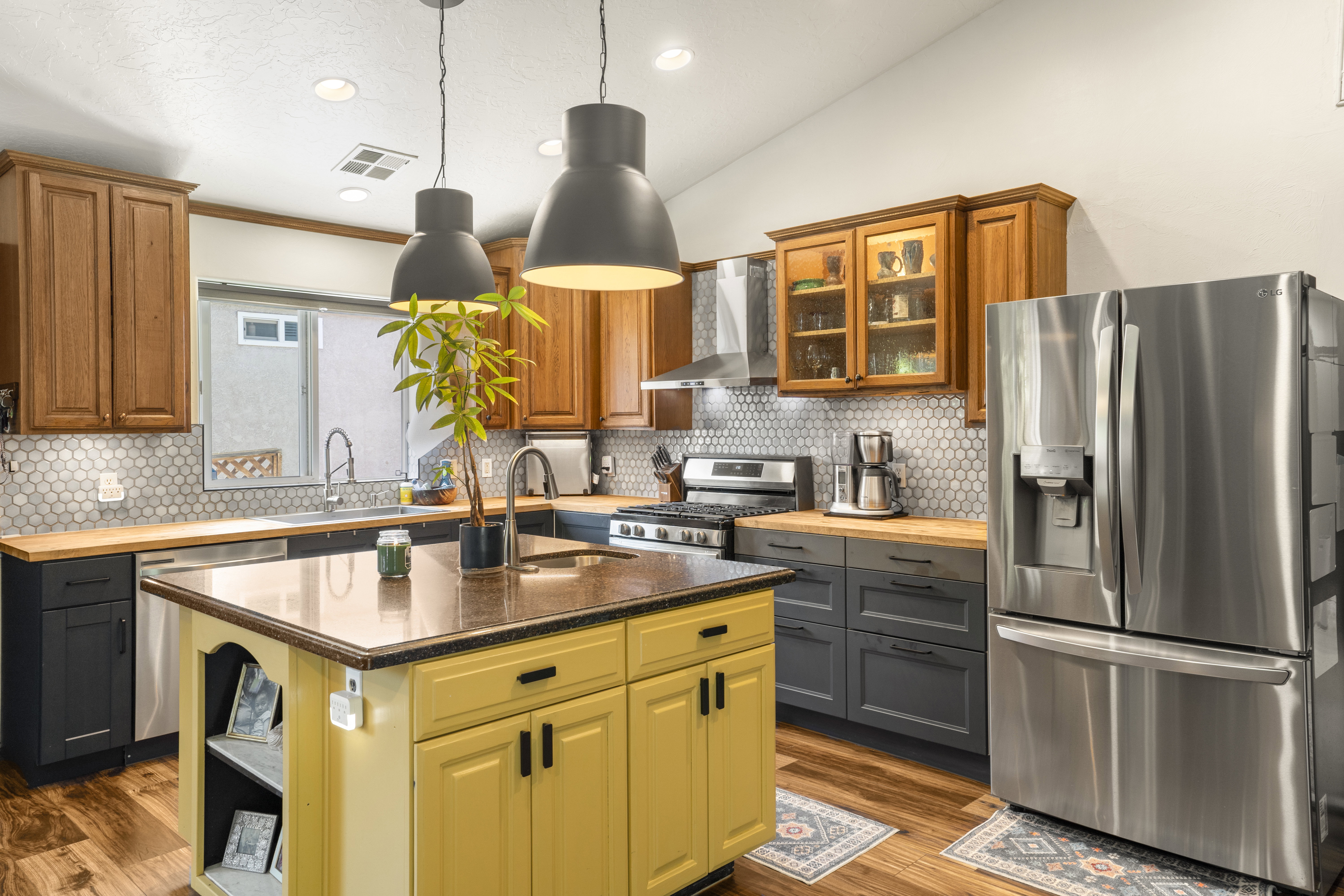 Two tone kitchen featuring stainless steel appliances, wooden counters, an island with sink, decorative light fixtures, and dark wood-style floors
