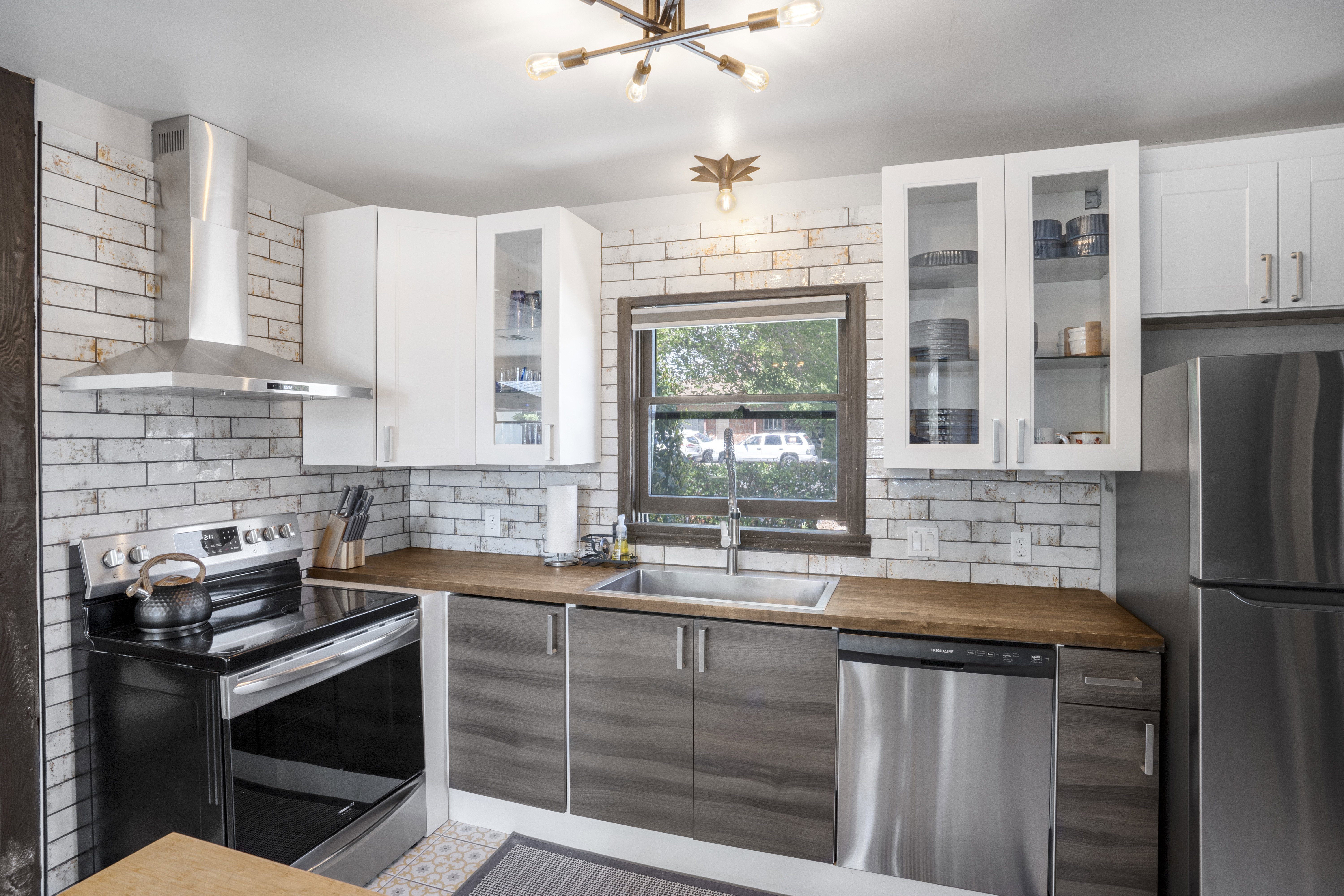 Kitchen with butcher block countertops, stainless steel appliances, glass fronted cabinets, two tone cabinetry, and tasteful backsplash