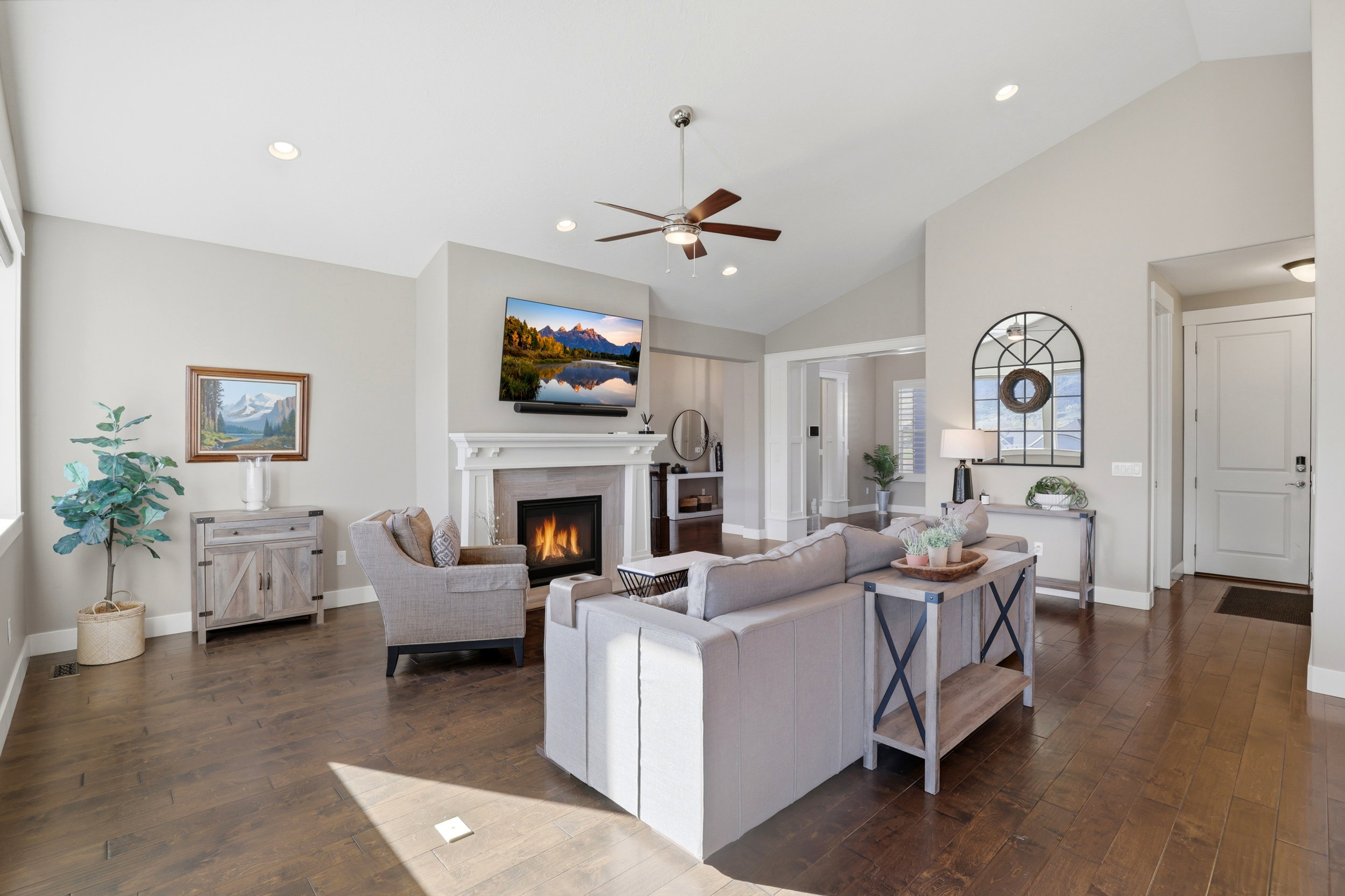 Living area with dark wood-style floors, a ceiling fan, a warm lit fireplace, lofted ceiling, and recessed lighting
