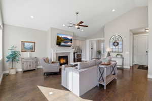Living area with dark wood-style floors, a ceiling fan, a warm lit fireplace, lofted ceiling, and recessed lighting