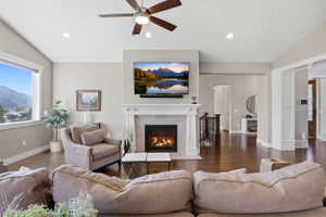 Living area with lofted ceiling, wood finished floors, a tile fireplace, a ceiling fan, and recessed lighting