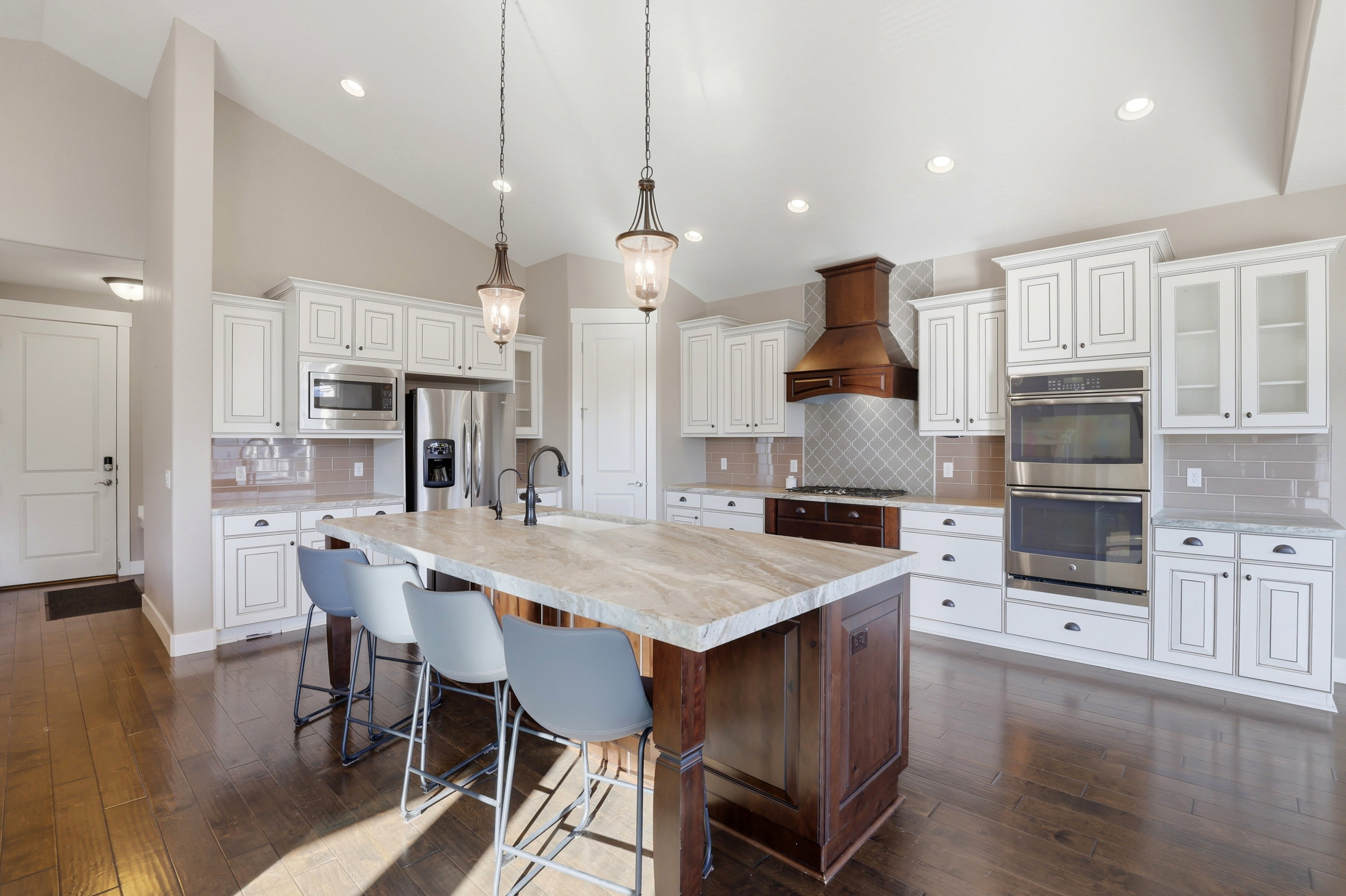 Kitchen with vaulted ceiling, stainless steel appliances, dark wood-style flooring, a kitchen breakfast bar, and a kitchen island with sink