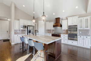 Kitchen with vaulted ceiling, stainless steel appliances, dark wood-style flooring, a kitchen breakfast bar, and a kitchen island with sink