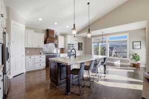 Kitchen with a breakfast bar, a center island with sink, two tone cabinetry, dark wood-style floors, and decorative backsplash