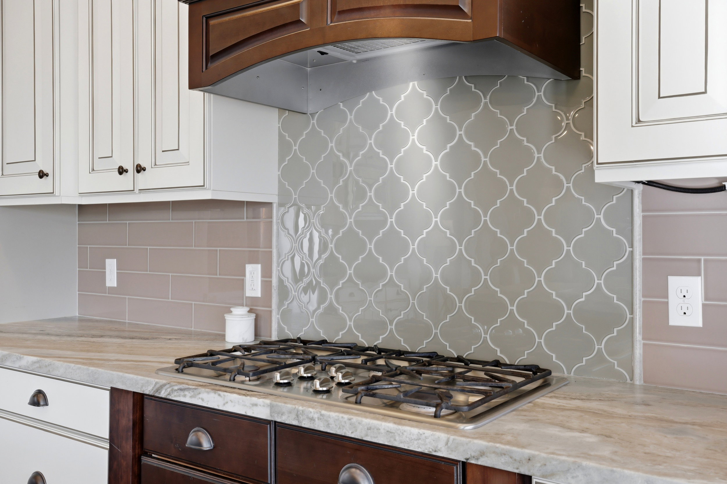 Kitchen with exhaust hood, light stone counters, white cabinetry, and stainless steel gas cooktop