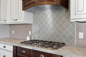Kitchen with exhaust hood, light stone counters, white cabinetry, and stainless steel gas cooktop