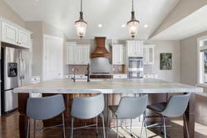 Kitchen featuring dark wood-type flooring, stainless steel appliances, a breakfast bar area, a large island, and vaulted ceiling