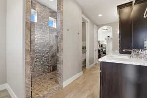 Bathroom featuring a walk in closet, vanity, wood finish floors, walk in shower, and tasteful backsplash