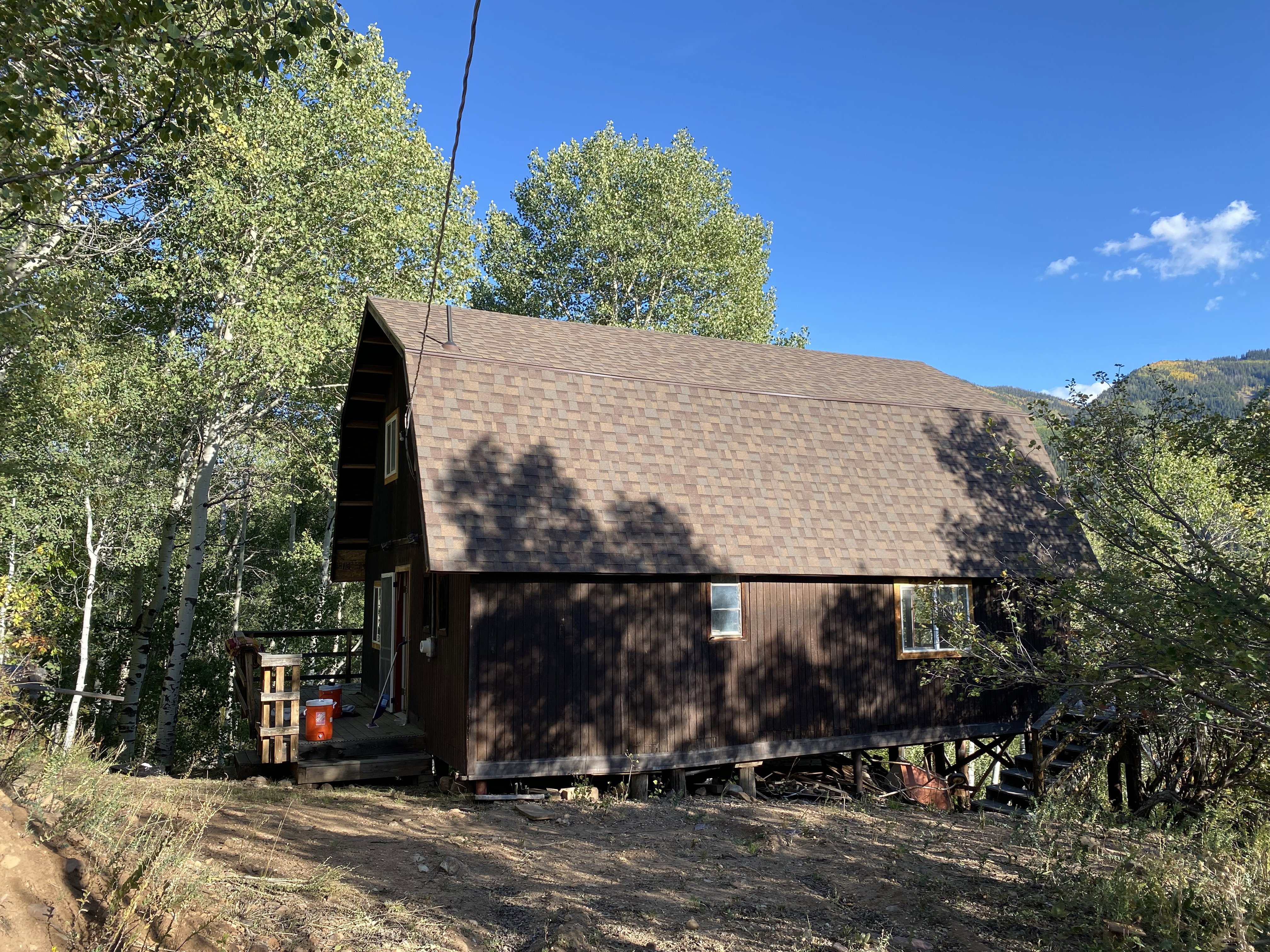 View of home's exterior featuring a gambrel roof, a shingled roof, and a wooden deck