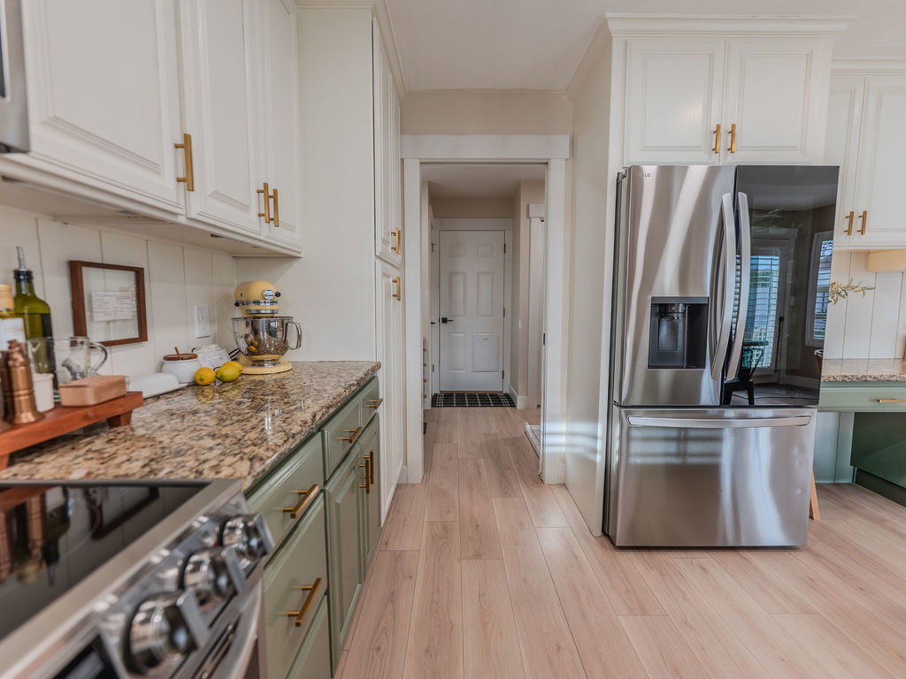 Two tone kitchen with stainless steel appliances, light stone counters, dual tone cabinetry, light wood-style floors, and tasteful backsplash