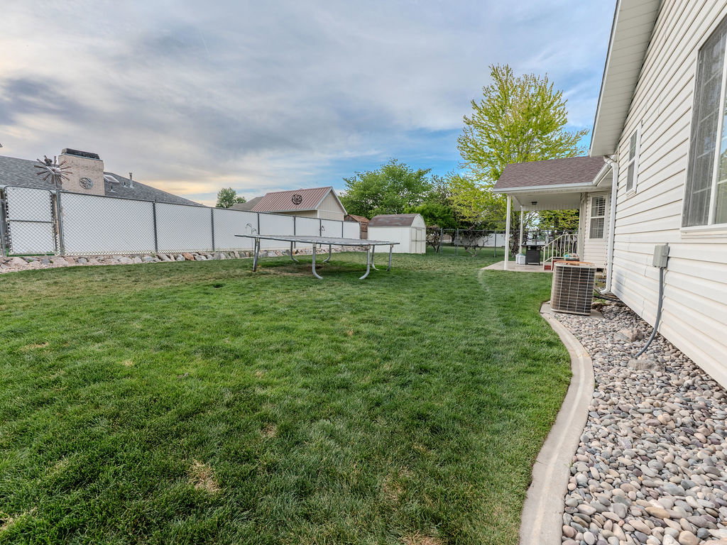 Fenced backyard featuring a trampoline and a storage shed