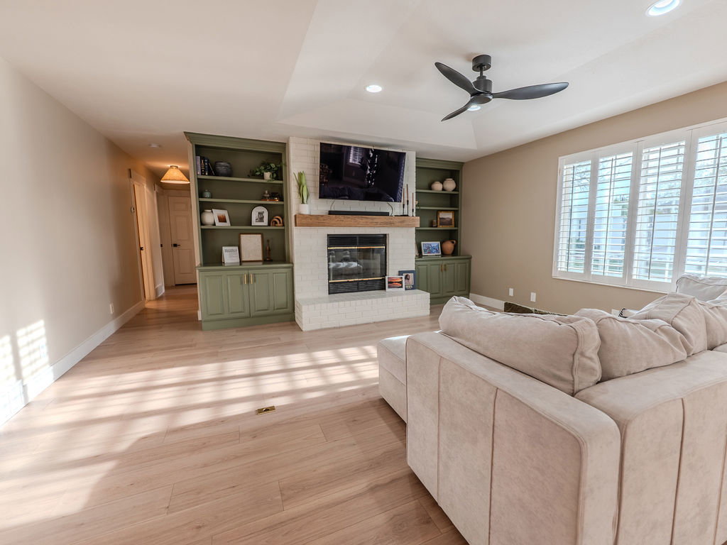 Living room with ceiling fan, light wood finished floors, a fireplace, built in shelves, and recessed lighting