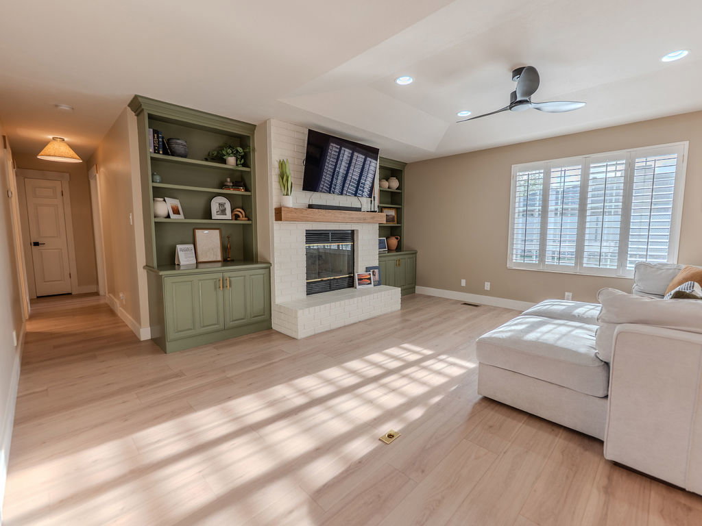 Living area with light wood-type flooring, a brick fireplace, a ceiling fan, built in features, and recessed lighting