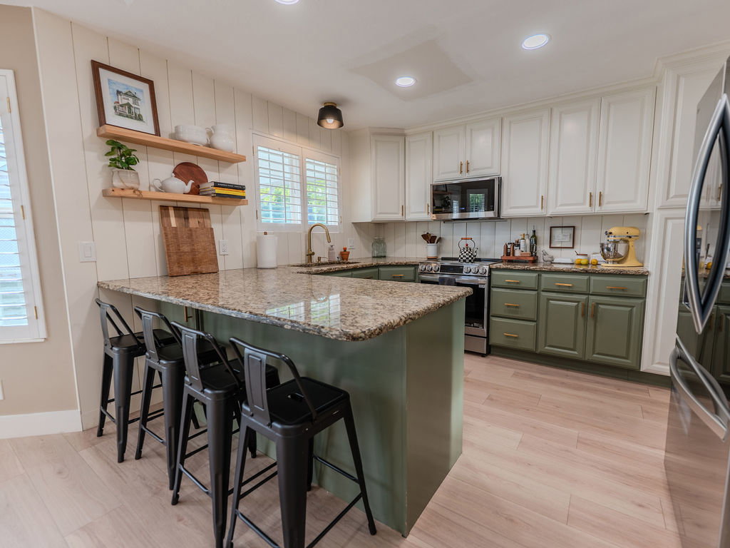 Kitchen with dual tone cabinets, a peninsula, light stone counters, a breakfast bar area, and stainless steel appliances