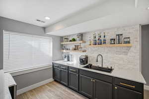 Lower level kitchenette featuring a double beverage refrigerator, sink, floating shelves and stone backsplash