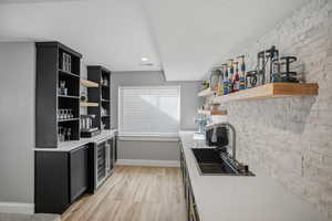 Lower level kitchenette featuring a double beverage refrigerator, sink, floating shelves and stone backsplash
