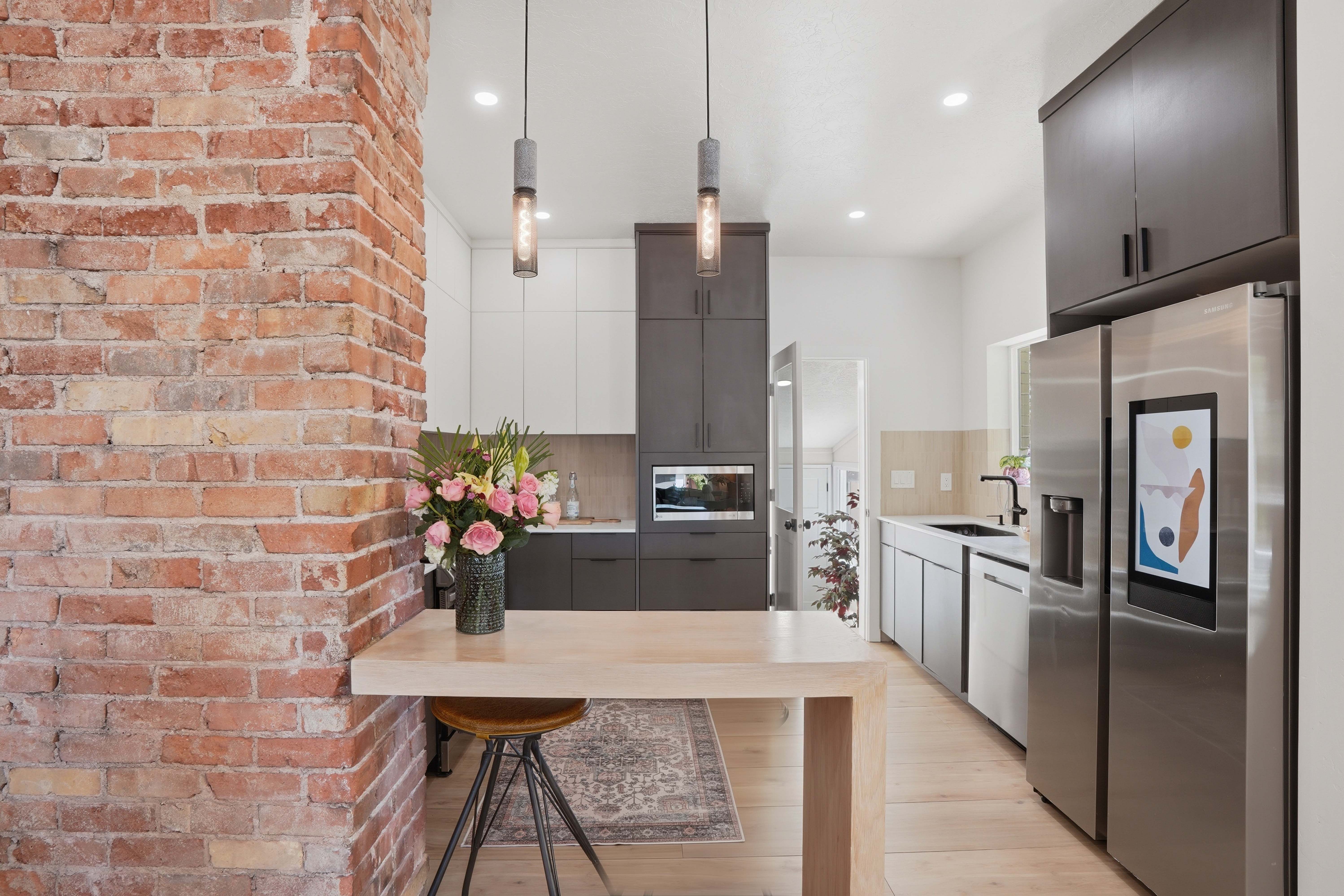 Kitchen with stainless steel appliances, dual tone cabinets, hanging light fixtures, and light porcelain glazed tile flooring