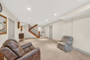 Spacious lower-level area featuring a wood staircase with black wrought iron spindles, recessed lighting, neutral carpeting, and a built-in cabinet with wood-finish doors