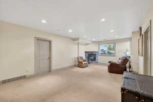 Spacious carpeted room featuring a stone-faced fireplace with a wood mantel, recessed lighting, and a window providing natural light