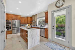 Kitchen with wood finish cabinetry, stainless steel appliances, light stone countertops, a kitchen island, and light tile patterned floors
