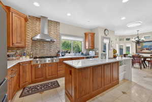 Kitchen with wood finish cabinets, a center island, light tile patterned flooring, light stone countertops, and tasteful backsplash