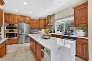 Kitchen with wood finish cabinets, stainless steel appliances, light stone countertops, a kitchen island, and light tile patterned floors