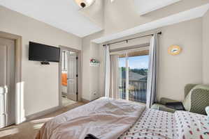 Carpeted room with a vaulted ceiling, a sliding glass door to an outdoor balcony, and a recessed doorway