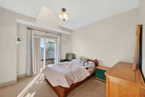 Carpeted room featuring a vaulted ceiling with a semi-flush mount light fixture, neutral wall paint, and a sliding glass door leading to a balcony with black railings