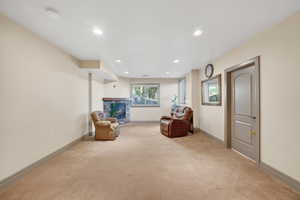 Spacious carpeted room featuring recessed lighting, a stone-faced fireplace with a wood mantle, and multiple windows