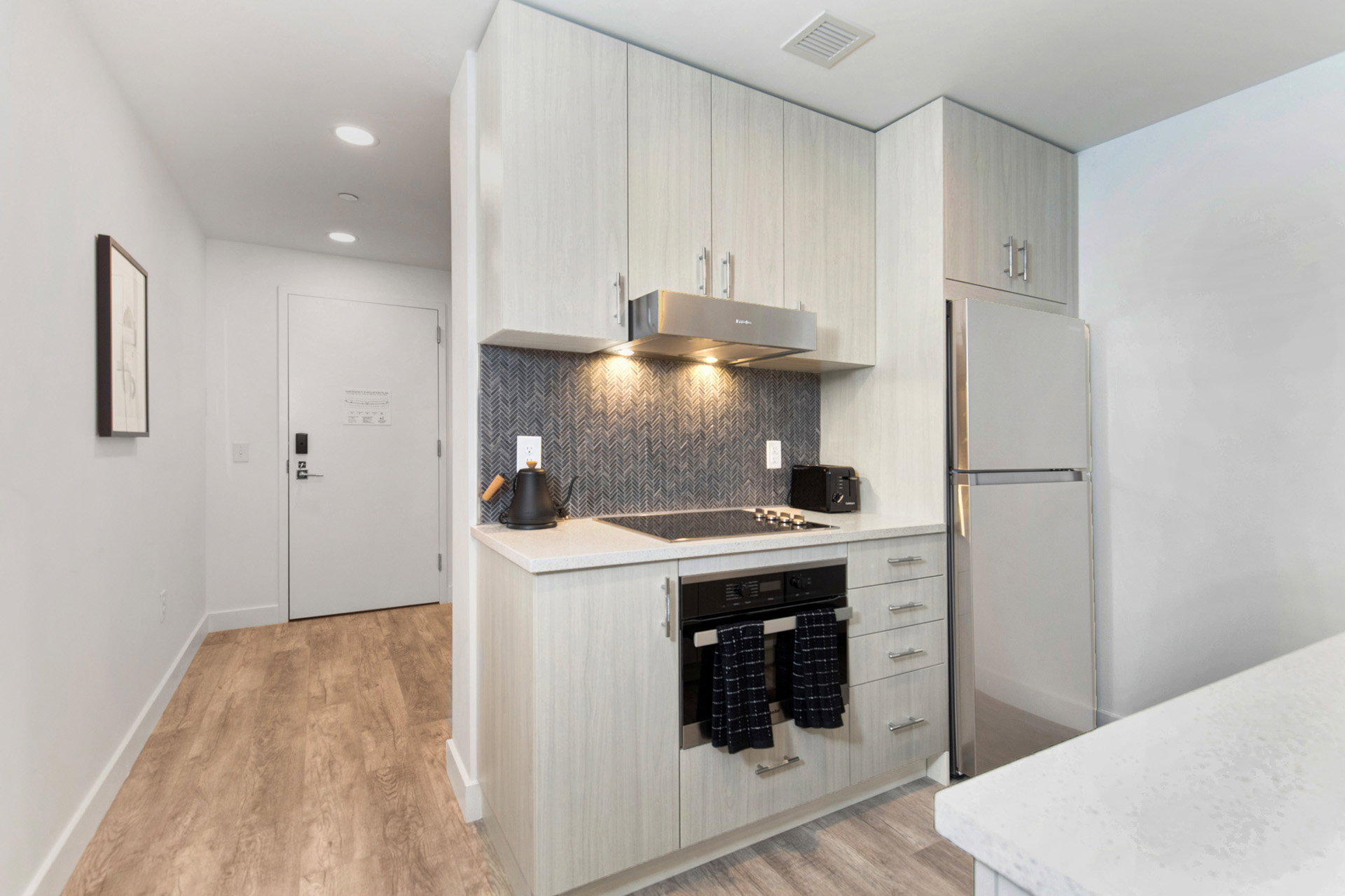 Kitchen featuring wall oven, freestanding refrigerator, light wood-style floors, tasteful backsplash, and light stone countertops