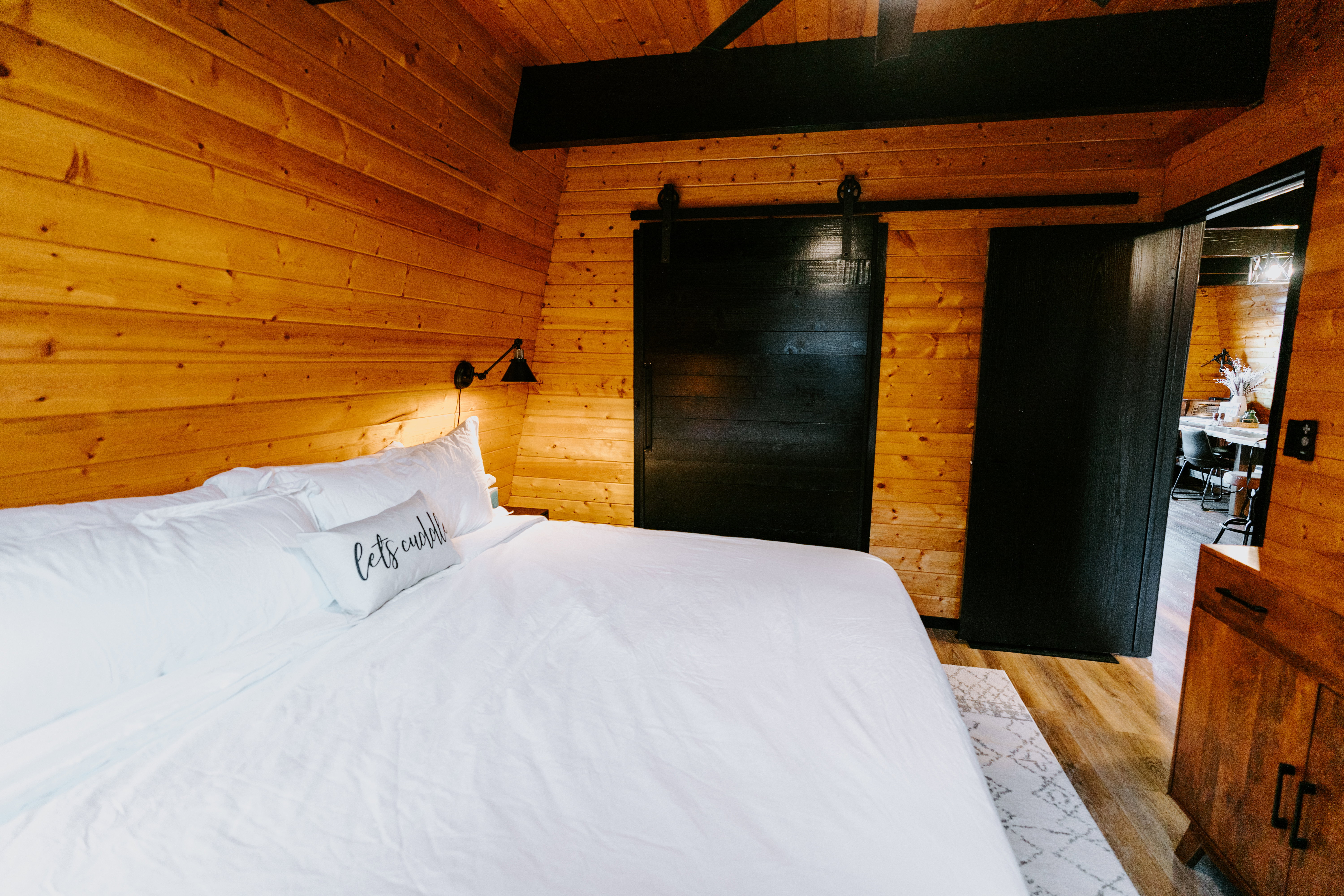 Bedroom with wood walls, ceiling fan, light wood-type flooring, a barn door, and a wood ceiling with exposed beams