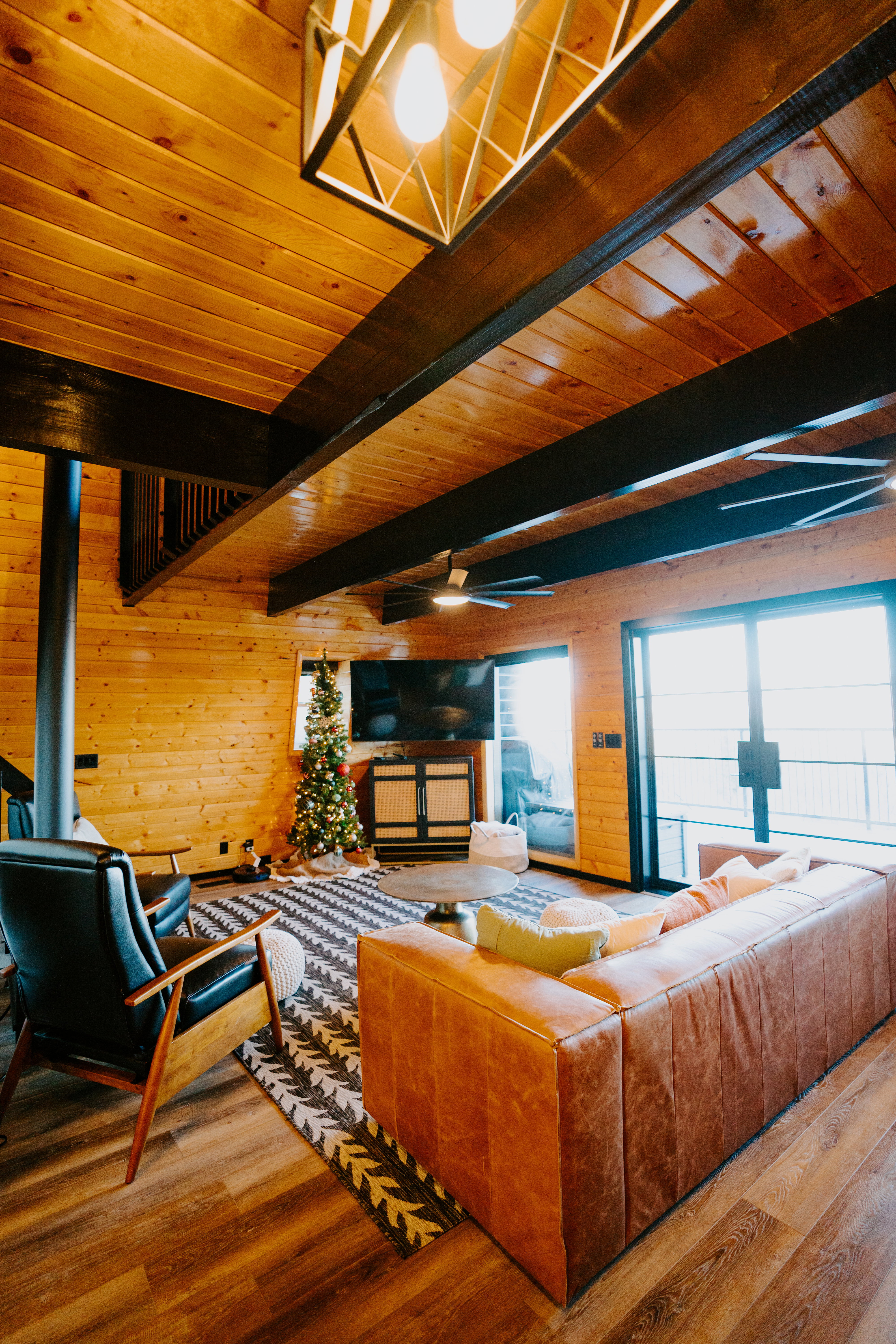 Living area featuring wooden walls, a wood ceiling with exposed beams, wood finished floors, ceiling fan, and a wood stove