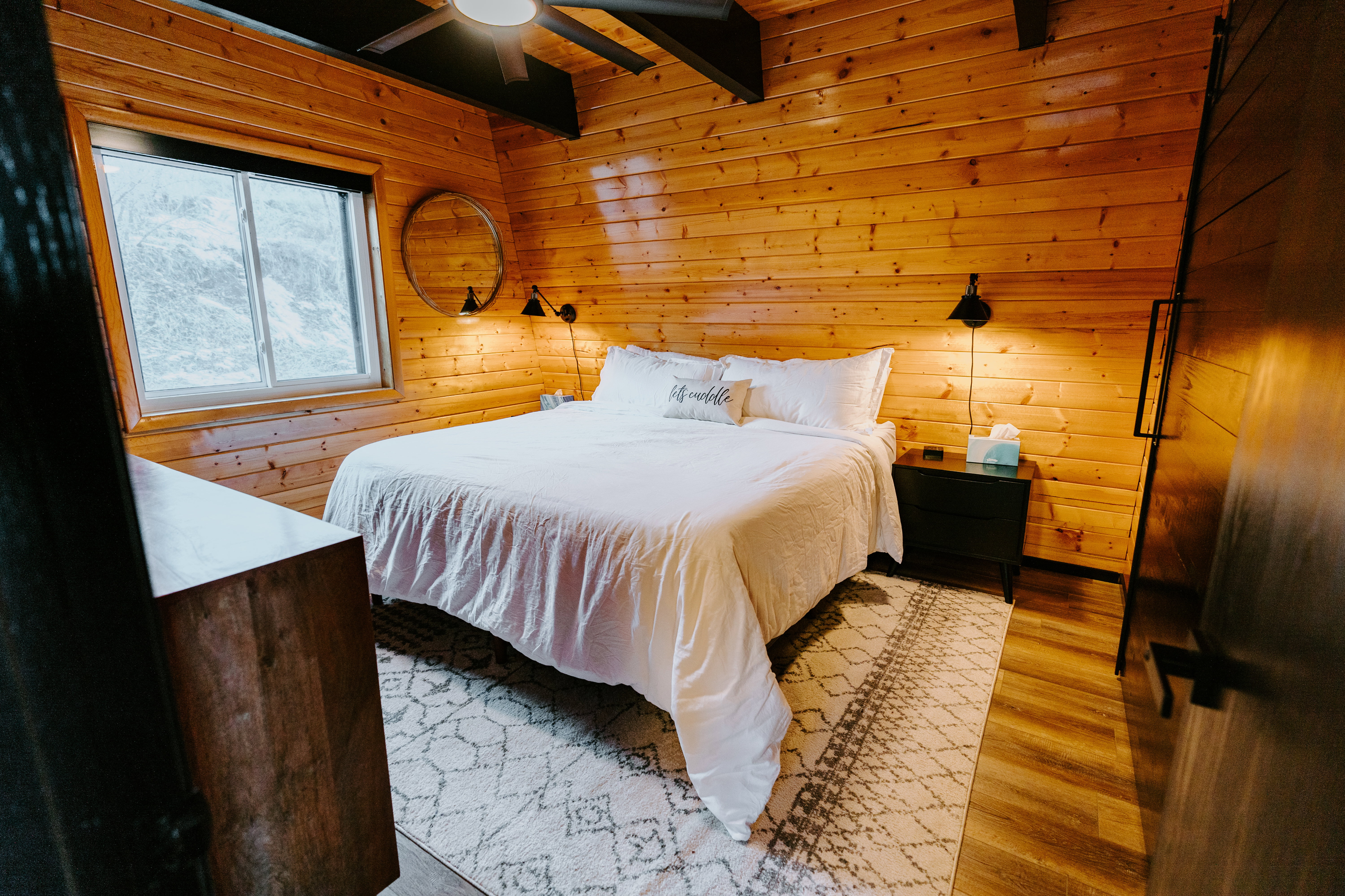 Bedroom with wooden walls, light wood-type flooring, beamed ceiling, and ceiling fan