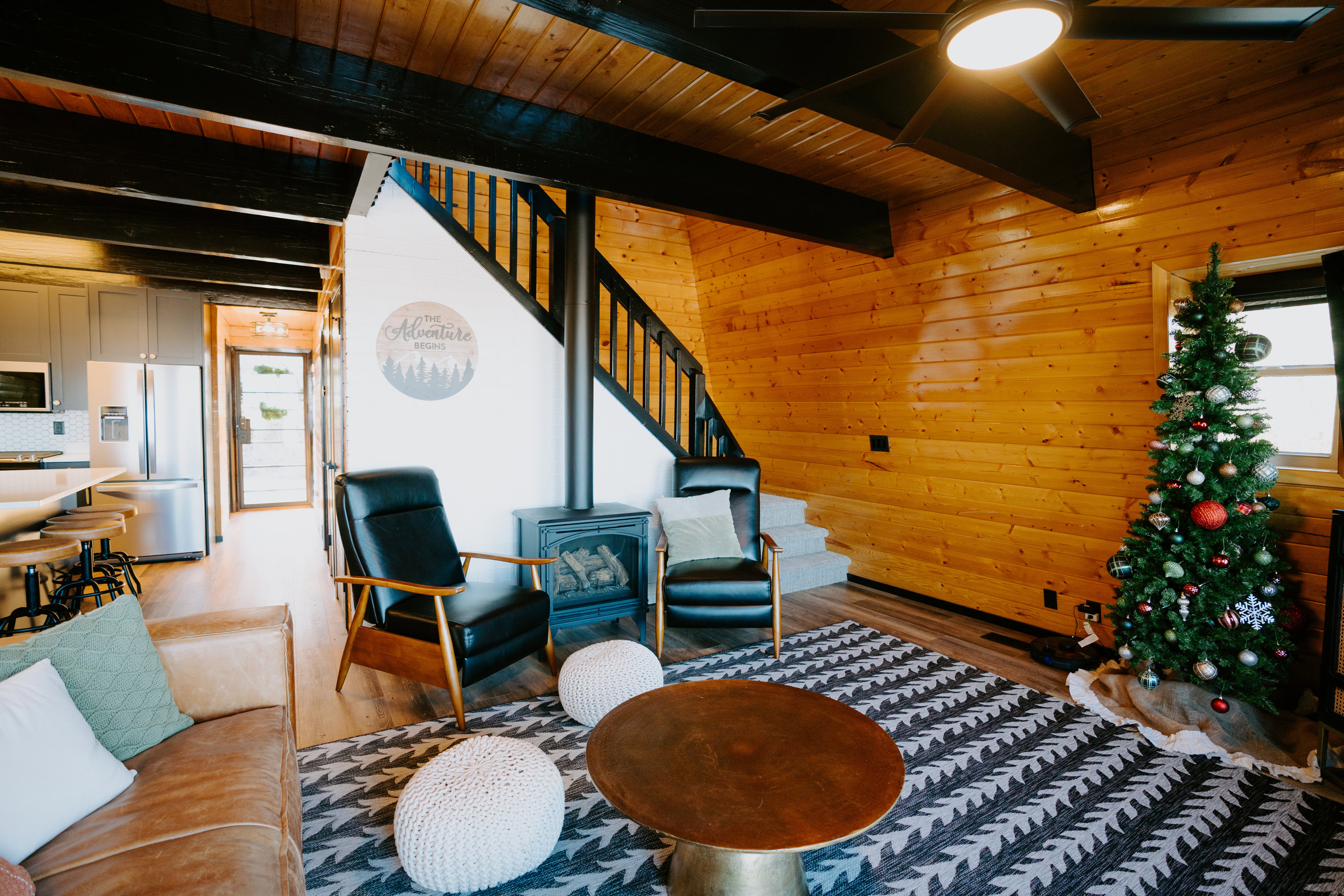 Living area with wood walls, a wood stove, wood finished floors, a wooden ceiling with exposed beams, and ceiling fan