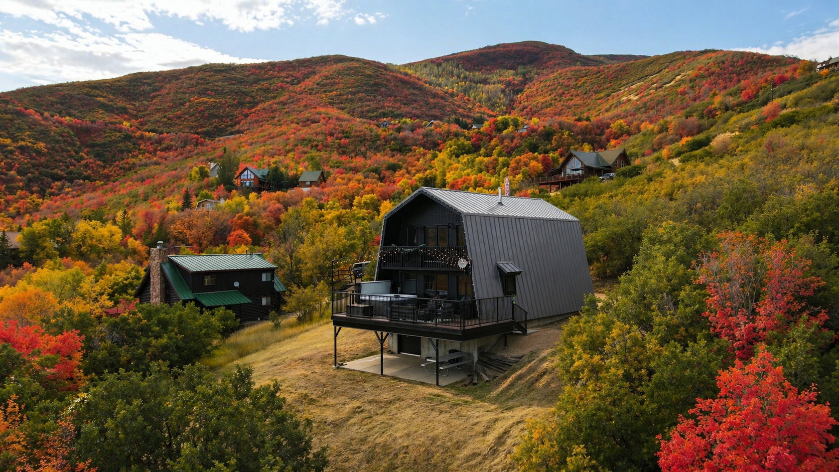Back of house with a chimney, a patio, a gambrel roof, a deck with mountain view, and a metal roof