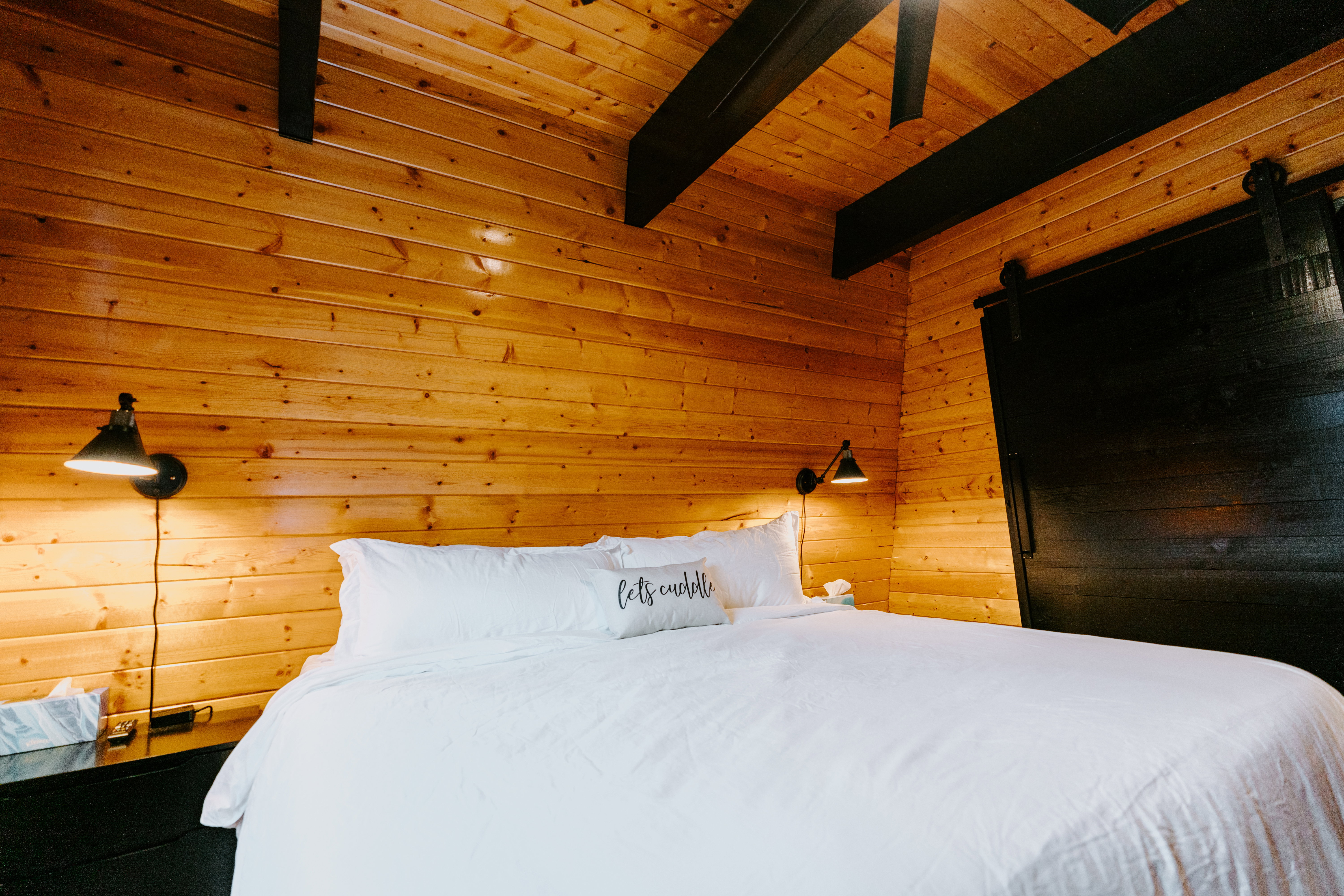Bedroom featuring wood walls, a wooden ceiling with exposed beams, and a barn door