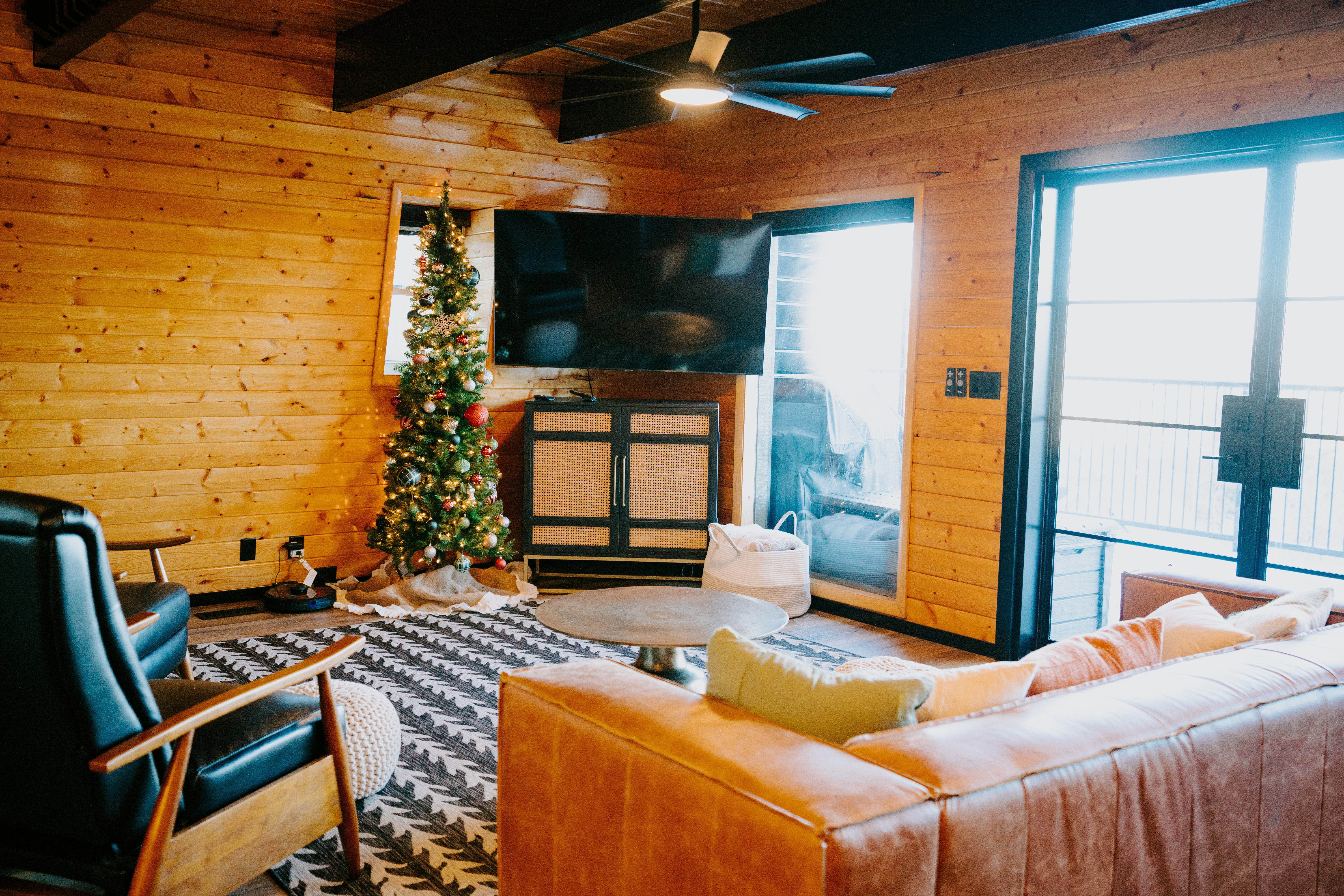Living room with wood walls, ceiling fan, wood finished floors, and a wood ceiling with exposed beams