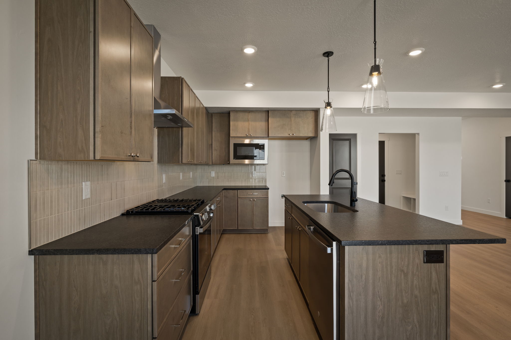 Kitchen with stainless steel appliances, a kitchen island with sink, light wood-style floors, decorative backsplash, and decorative light fixtures