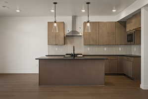 Kitchen featuring an island with sink, dark wood-type flooring, hanging light fixtures, dark stone counters, and backsplash