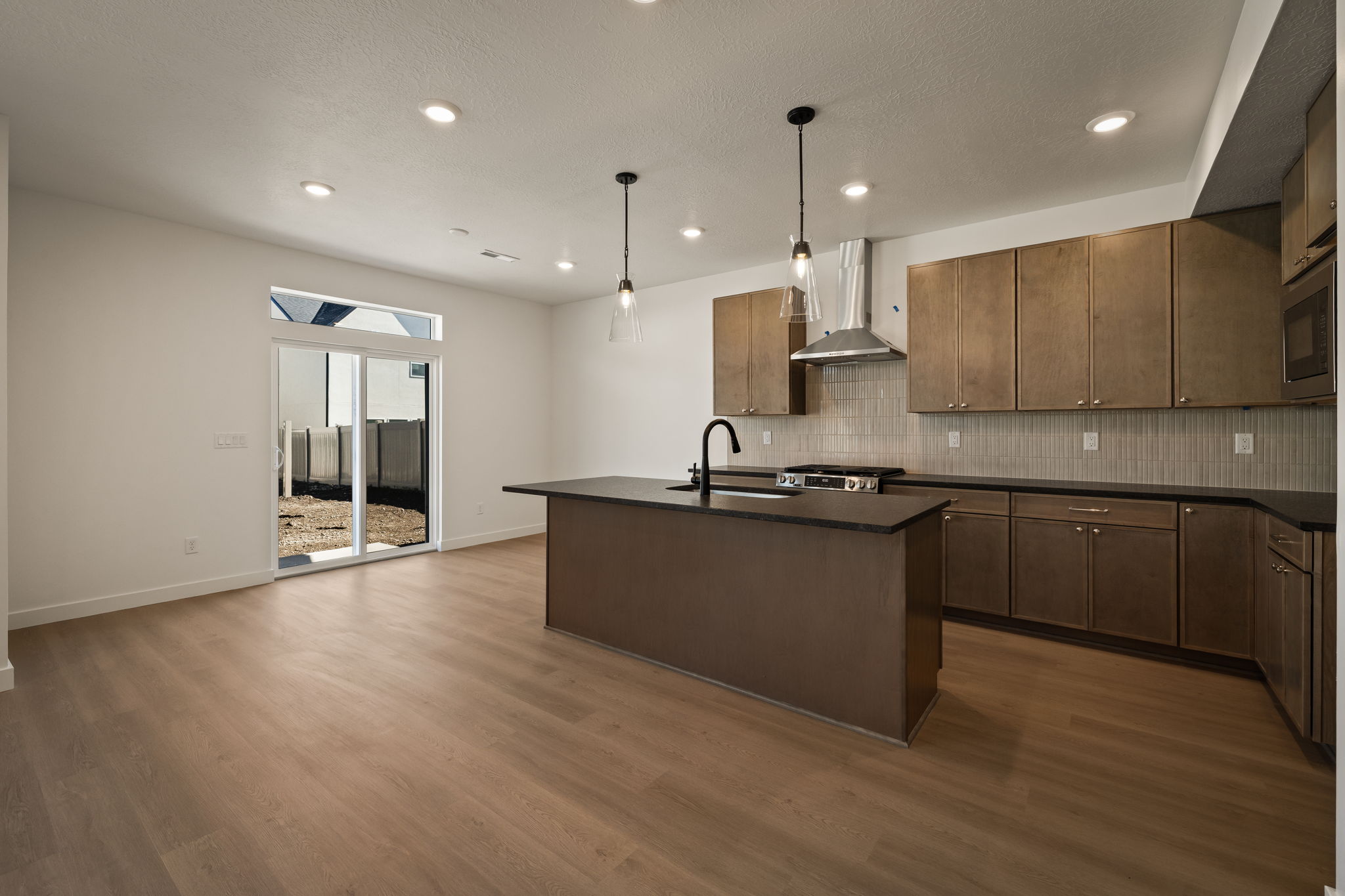 Kitchen with a center island with sink, decorative light fixtures, dark wood-style flooring, and stainless steel appliances
