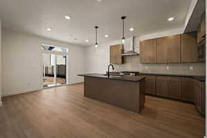 Kitchen with a center island with sink, decorative light fixtures, dark wood-style flooring, and stainless steel appliances