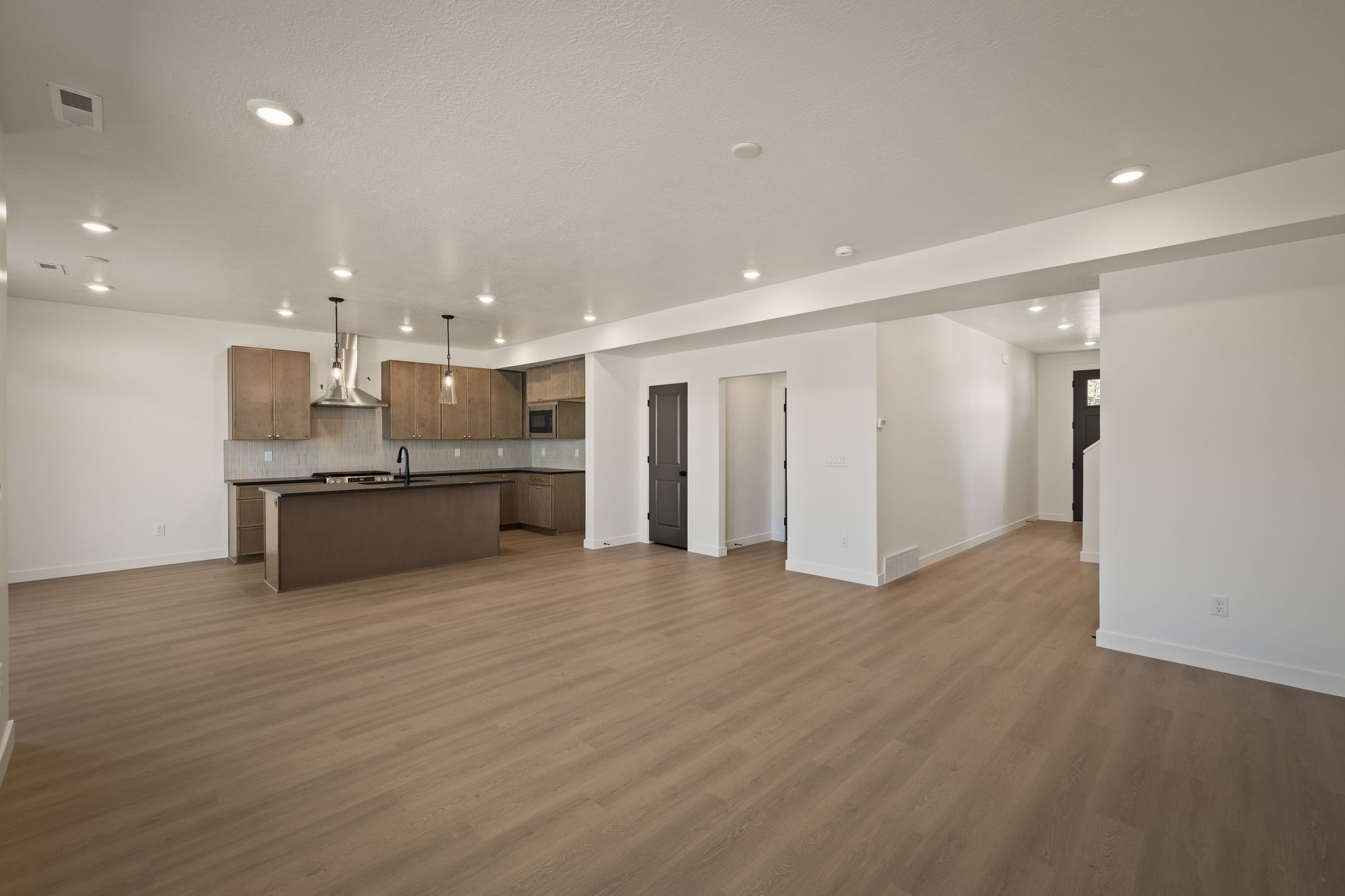 Kitchen with open floor plan, a kitchen island with sink, dark countertops, backsplash, and decorative light fixtures