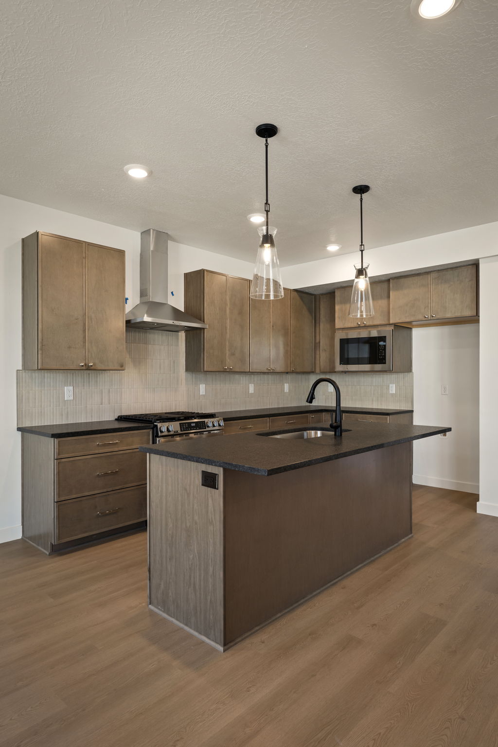 Kitchen with a kitchen island with sink, hanging light fixtures, dark wood finished floors, and dark stone counters
