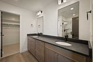 Full bath featuring double vanity, a marble finish shower, a walk in closet, recessed lighting, and dark wood-style flooring