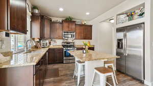 Kitchen with dark wood finish cabinets, stainless steel appliances, a breakfast bar area, light stone countertops, and recessed lighting