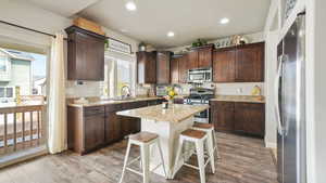 Kitchen featuring dark wood finish cabinetry, a kitchen bar, stainless steel appliances, light wood-style flooring, and recessed lighting