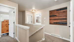 Top of stairway with carpet flooring, an upstairs landing, and a textured ceiling