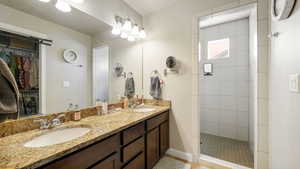 Master bathroom featuring double vanity, tiled shower, and a spacious closet