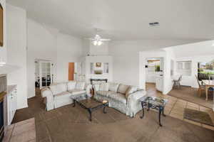Living room with dark tile patterned flooring, vaulted ceiling, dark colored carpet, a fireplace, and a ceiling fan