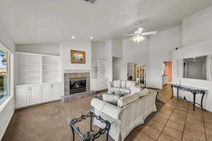 Living area with ceiling fan, vaulted ceiling, a fireplace, tile patterned flooring, and built in shelves